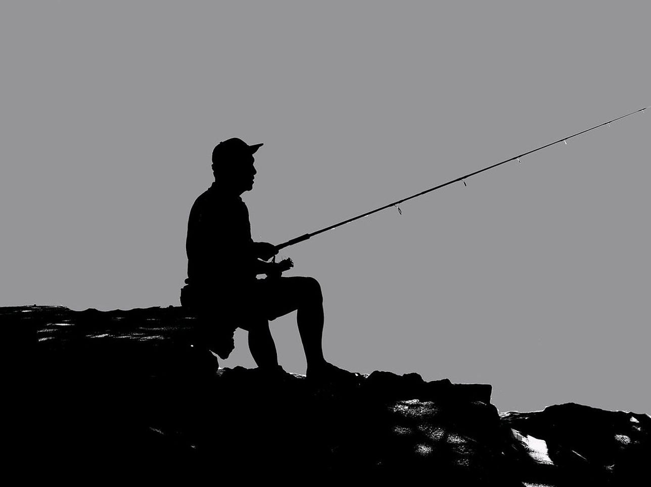 Freshwater angler holding a bass, with fishing rod and net resting on the river bank